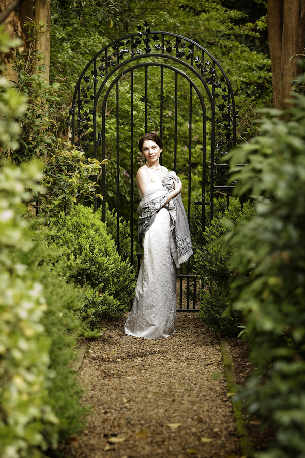 beautiful bride wearing ivory s-line style dress holding a silver shawl around her in front of garden gate - photo by North Carolina based wedding photographers Cunningham Photo Artists